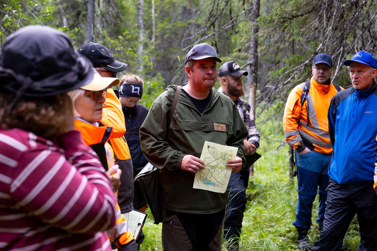 Kari-Pekka Poutanen metsäalan opiskelijoidenkanssa metsässä kädessään paperi.