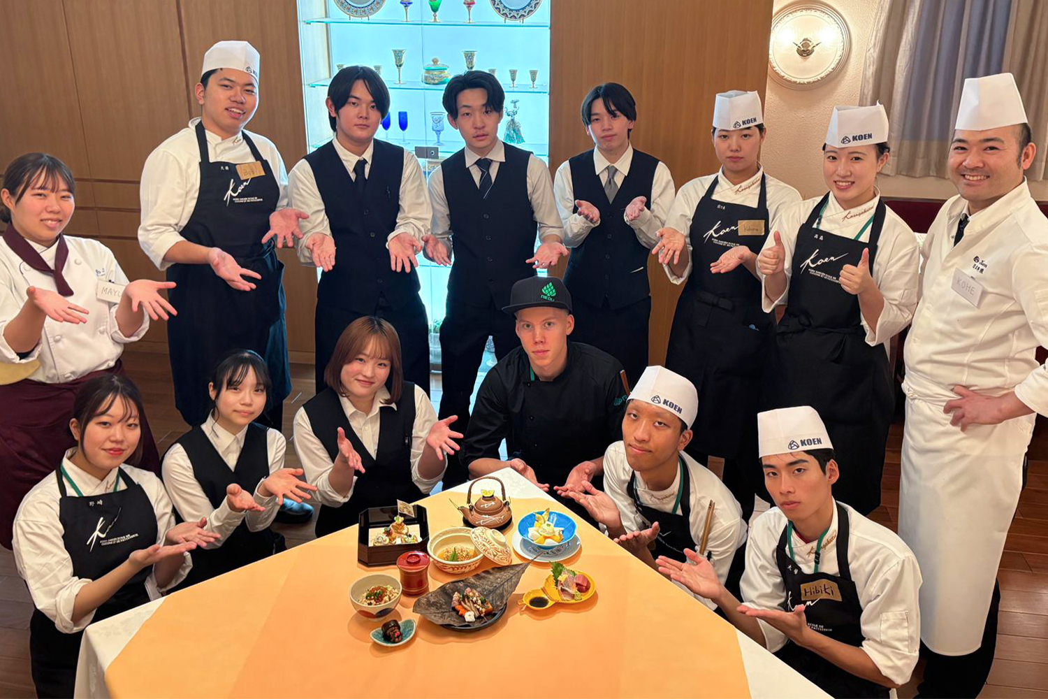 Opiskelijat ovat kerääntyneet esittelemään pöydän ääreen annoksia, jotka ovat tehneet.