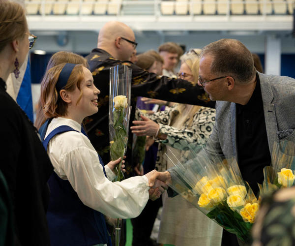 Opiskelija ottaa vastaan kukan ja kättelee valmistujaisissa.