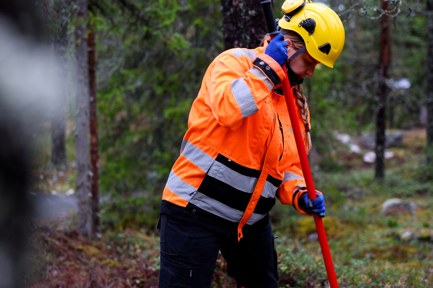 Nainen rakentamassa pyöräreittiä varrellisen työkalun kanssa oransseissa työvaatteissa.