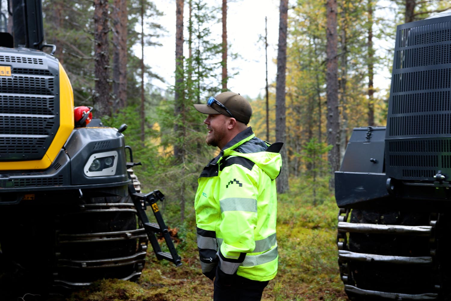 Jari Laine kävelemässä metsässä kahden metsäkoneen välissä.