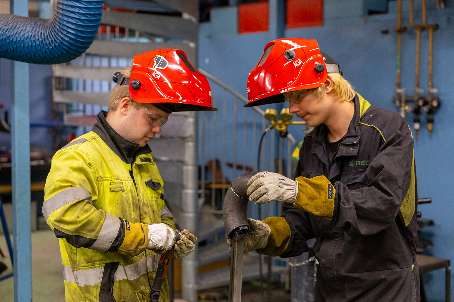 Niilo ja Sammeli punaiset hitsauskypärät päässä suojavarusteissa katsovat metallinpalaa.