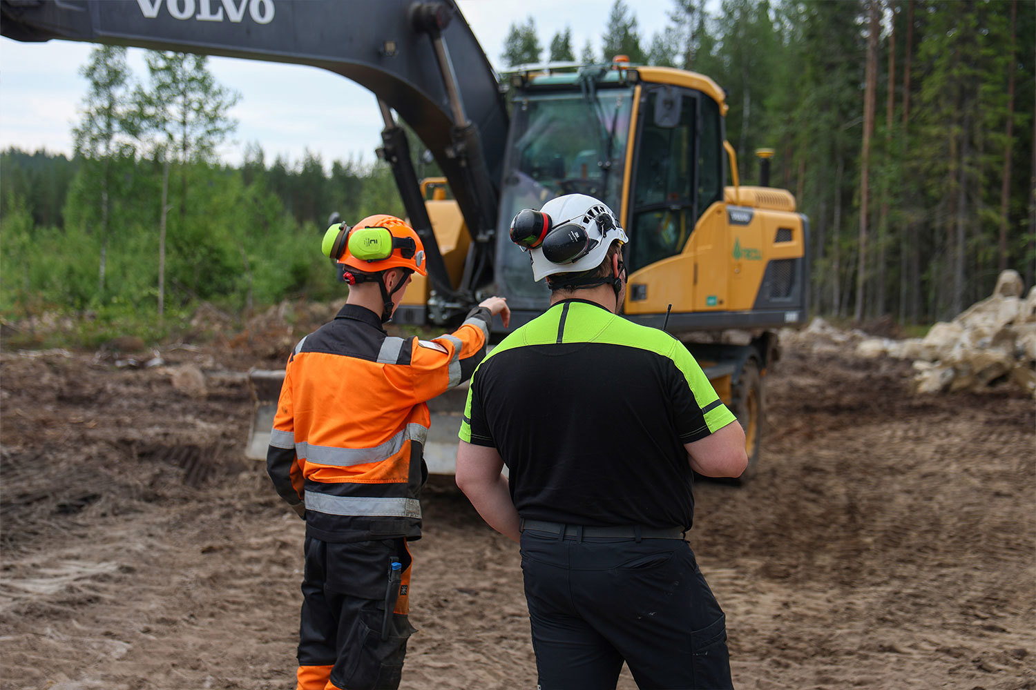 Maanrakennusalan opiskelija ja ohjaaja keskustelevat työmaalla kaivinkoneen vieressä Tuomijärven ajoharjoitteluradan rakennustöiden aikanaMaanrakennuskoneenkuljettajaksi opiskeleva Tuomas Leskelä työskentelee kaivinkoneen ohjaamossa ajoharjoitteluradan rakennustyömaalla.